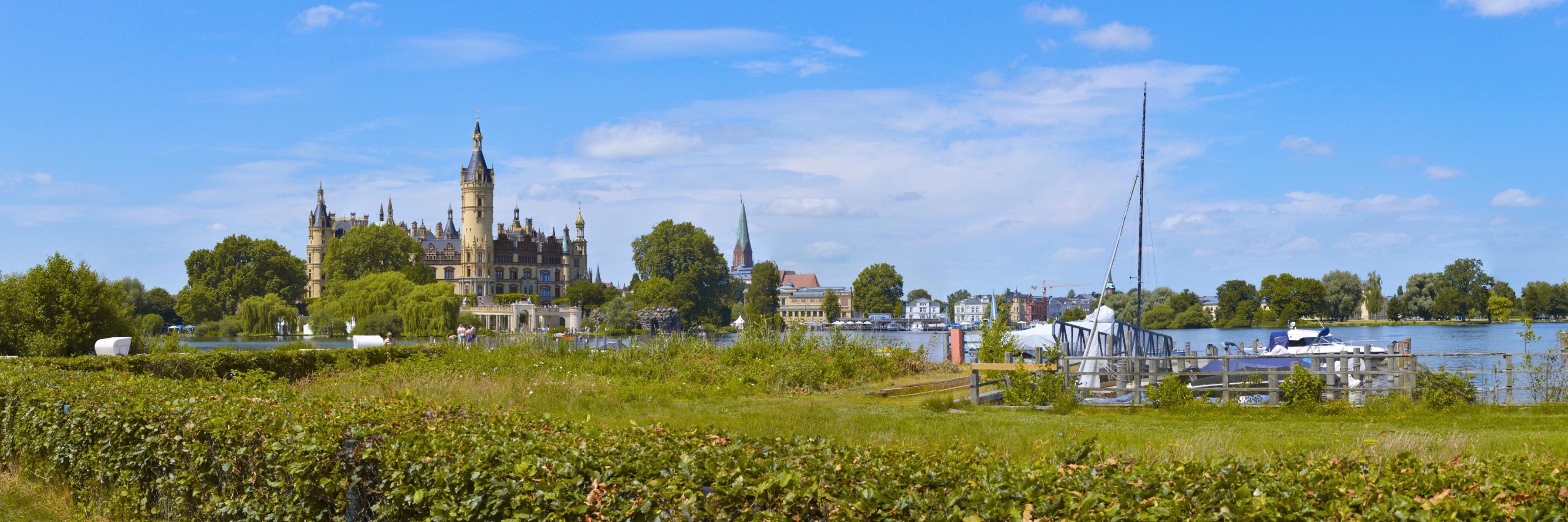 Panoramablick auf das Schweriner Schloß von der Schlossbucht aus mit Anlegehafen, Schiffen und blauem Himmel