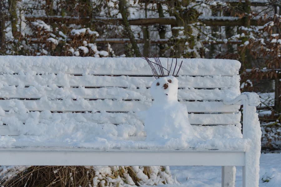 Kleiner Schneemann auf Parkbank im Winter